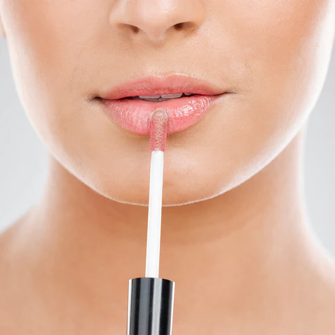 Close-up of a woman applying nude lip gloss.