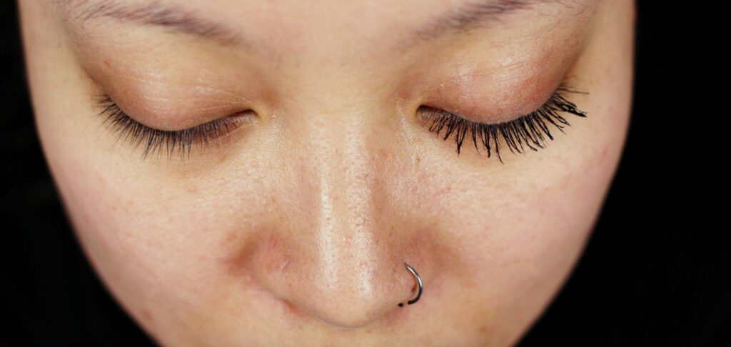 Close-up of a person's nose with a nose ring and long eyelashes.