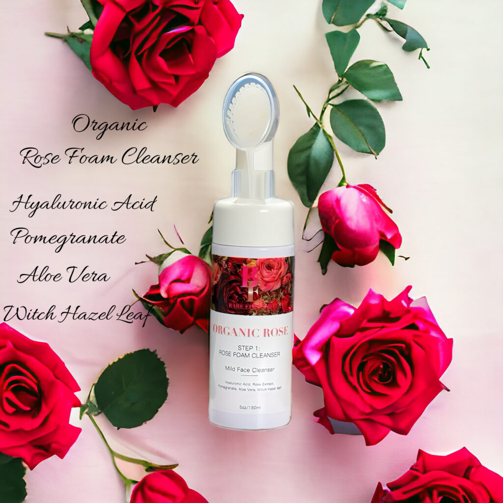 A bottle of rose water surrounded by fresh red roses on a white surface.