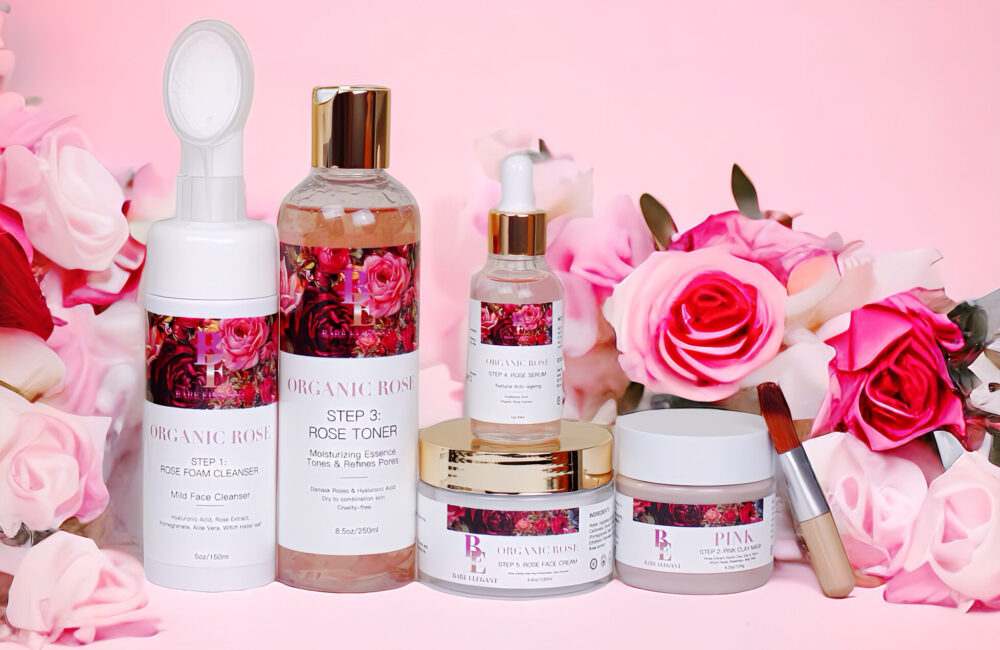 A collection of pink rose-themed skincare products arranged with fresh roses on a pink background.