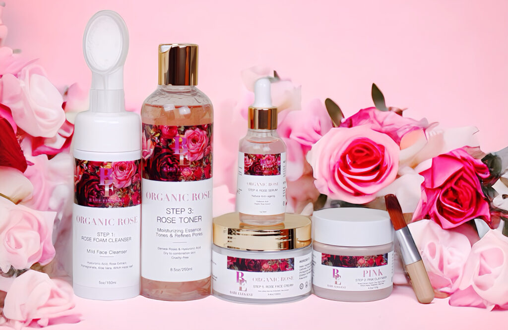 A collection of pink rose-themed skincare products arranged with fresh roses on a pink background.