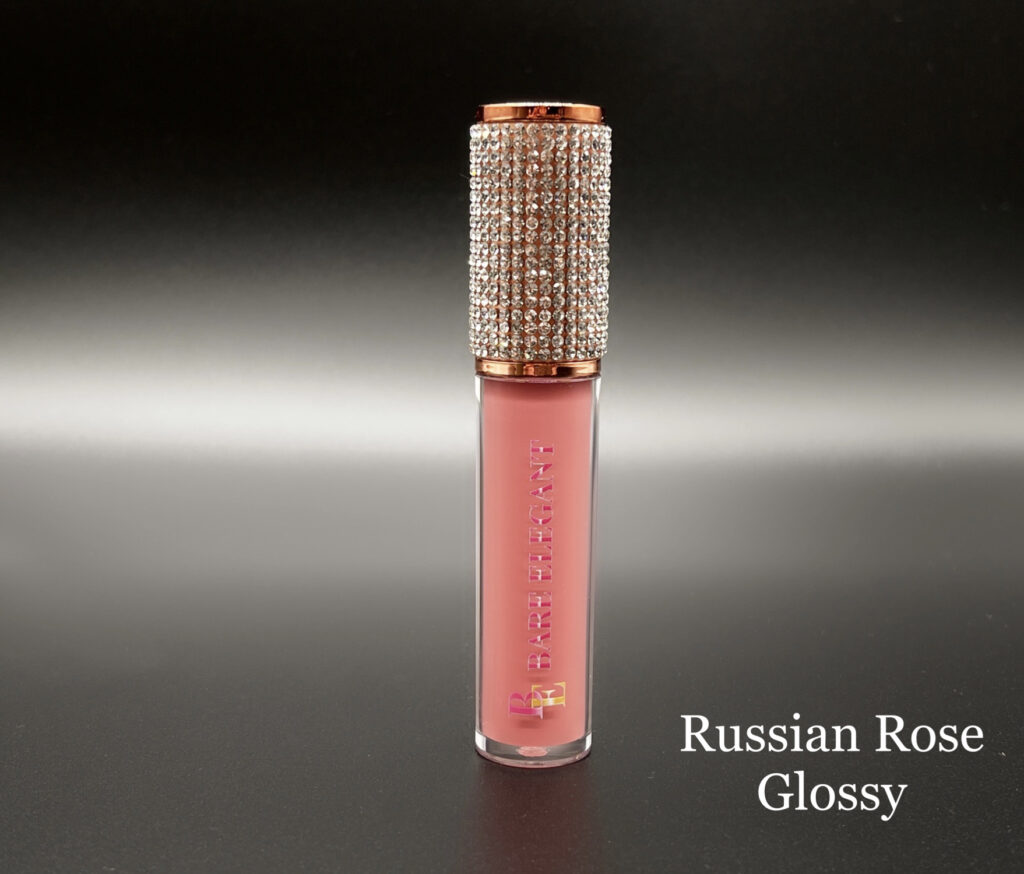 Glossy pink lip gloss with a sparkling cap on a reflective surface.