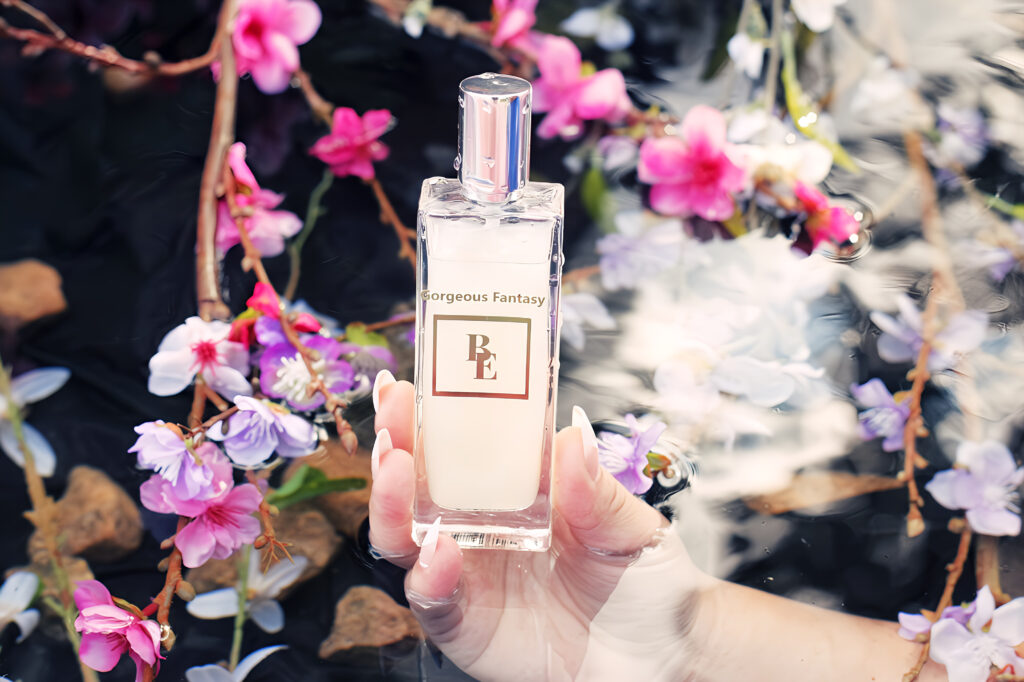Hand holding a perfume bottle surrounded by pink blossoms.