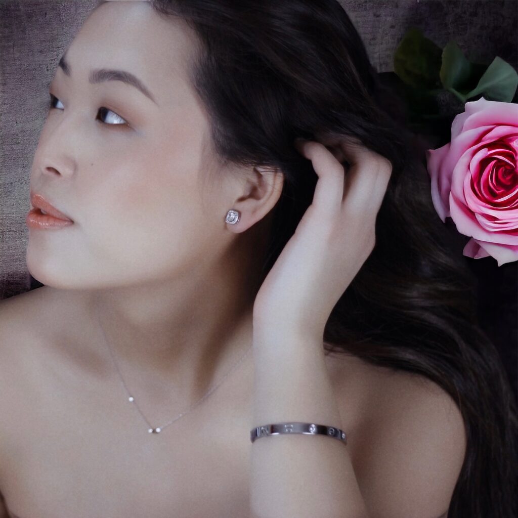 A woman gently touching her hair with a pink rose beside her.